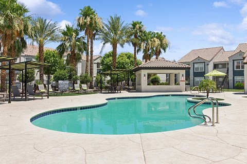 Dog-Friendly Apartments in East Las Vegas NV - Monterra - Resort Style Swimming Pool With Palm Trees, Lounge Chairs, Shaded Seating, And Community Buildings Under Blue