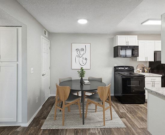 Model Dining Room with Wood-Style Flooring and View of Kitchen with White Cabinets at Solano Springs Apartments located in Tucson, AZ.