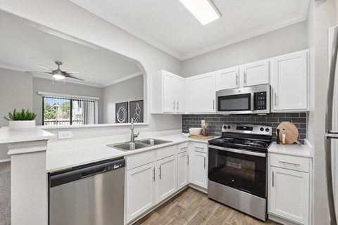 Model Kitchen with White Cabinets, Wood-Style Flooring and View of Living Room at Hidden Creek Apartments located in Lewisville, TX.