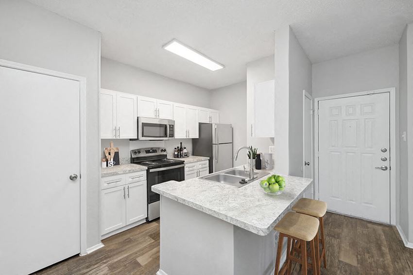 Model Kitchen with White Cabinets and Wood-Style Flooring at Heatherstone Apartments in Dallas, TX.