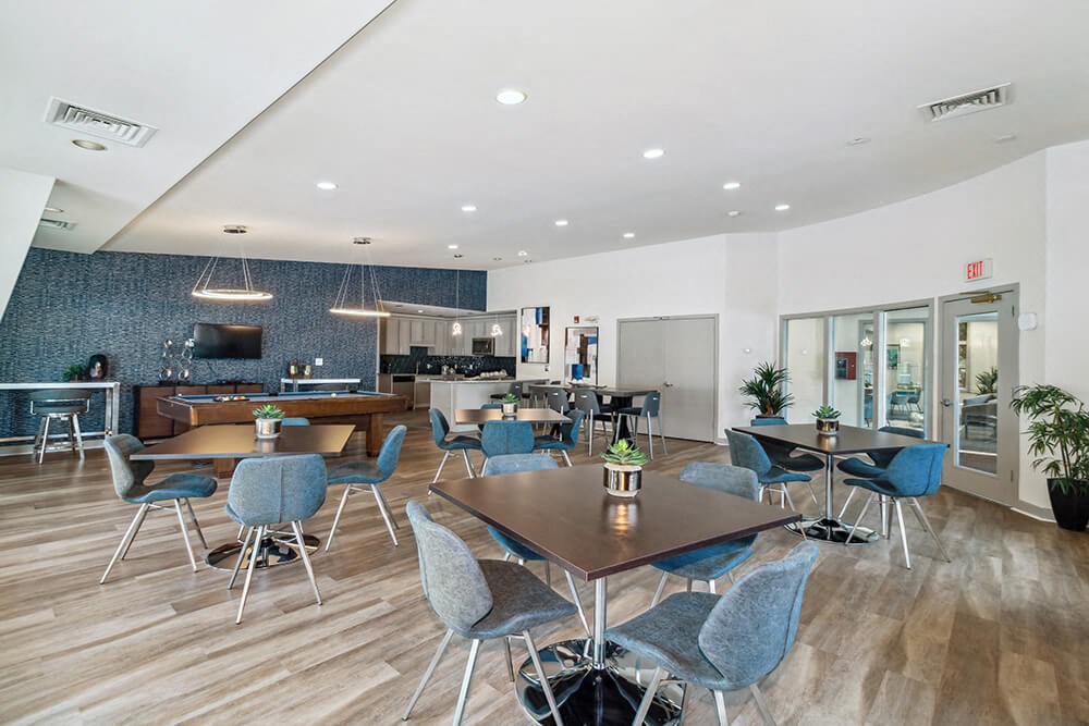 Community area with tables and chairs and a kitchen in the background