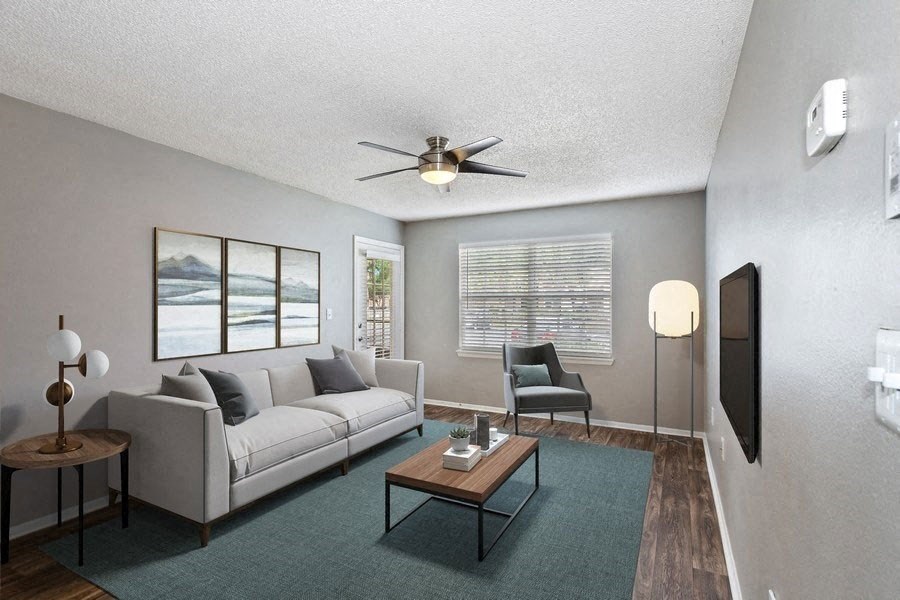 Model living room with wood floors and large carpet rug under furniture and patio door in back
