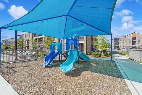 Community Playground with Slides and Blue Canopy at Alta 3Eighty Apartments located in Aubrey, TX.