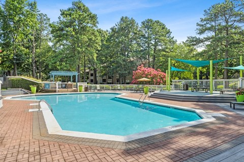 Pet-Friendly Apartments in Marietta, GA - Element 41 - A Swimming Pool With Brick Paver Deck, Shade Sails, Lounge Seating, And Lush Trees Under A Clear Blue Sky.