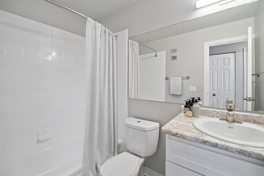 Model Bathroom with Bathtub/Shower, Wood-Style Flooring & White Cabinets at Waterfront Apartments in Lakewood, CO.