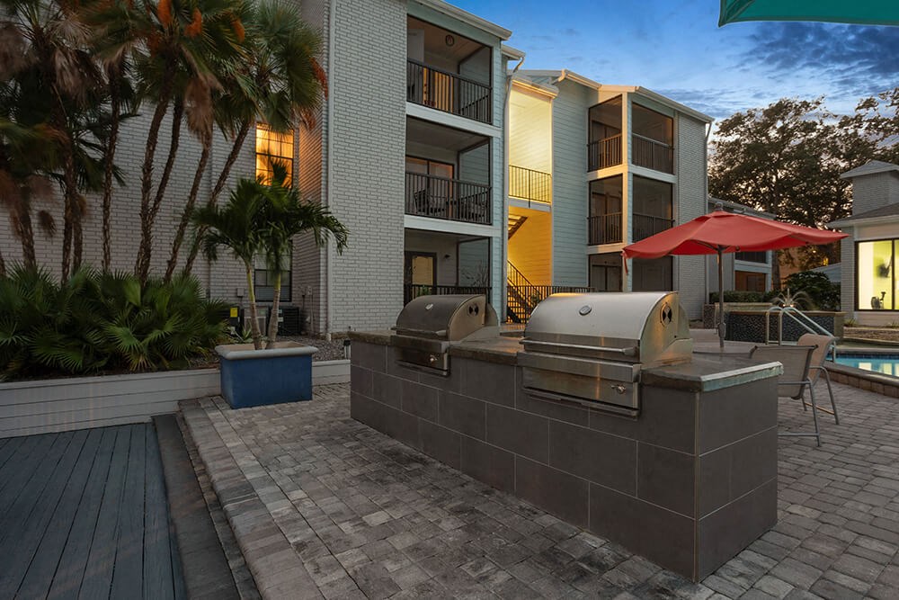 Outdoor BBQ Area with Furniture and Pool View at Haven at Water's Edge Apartments in Tampa, FL.