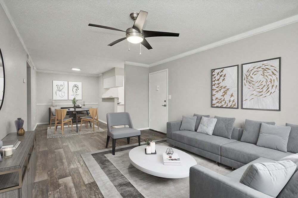 Model Living Room with Wood-Style Flooring and View of Kitchen/Dining Area at Carrollwood Station Apartments in Tampa, FL.