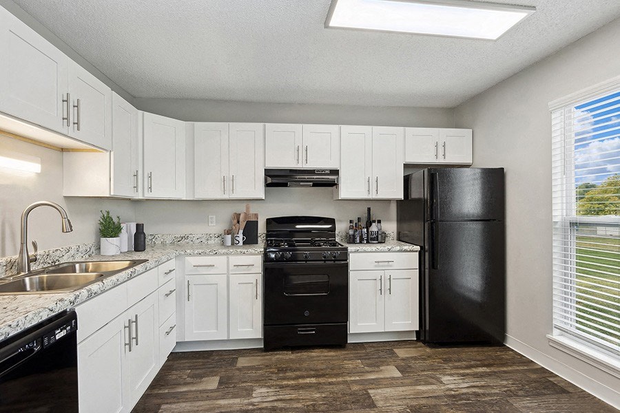 Model Kitchen with White Cabinets, Wood-Style Flooring and Window View at Parc at Creekside Apartments in Kansas City, MO.