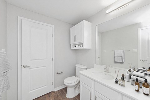Model Bathroom with White Cabinets and Wood-Style Flooring at Hidden Creek Apartments located in Lewisville, TX.