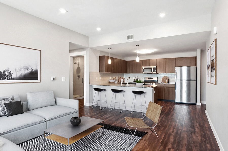 Model Living Room with Wood-Style Flooring and View of Kitchen at Seven Skies Apartments located in Sandy, UT.