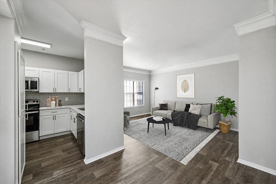 Model Kitchen with White Cabinets, Wood-Style Flooring and View of Living Room at Bridges at Oakbend Apartments located in Lewisville, TX.