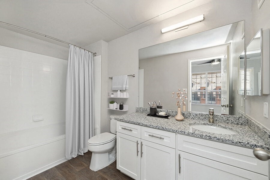 Model Bathroom with White Cabinets, Wood-Style Flooring and Shower/Tub at Chapel Hill Apartments in Lewisville, TX.