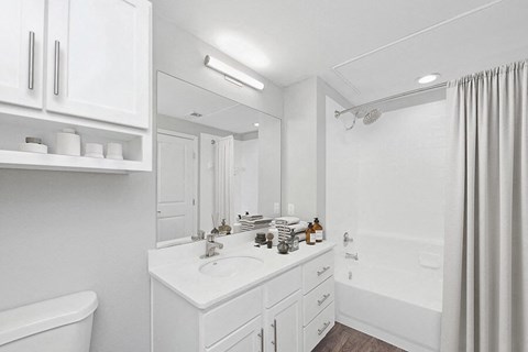 Model Bathroom with White Cabinets, Wood-Style Flooring & Shower/Tub at Hidden Creek Apartments located in Lewisville, TX.