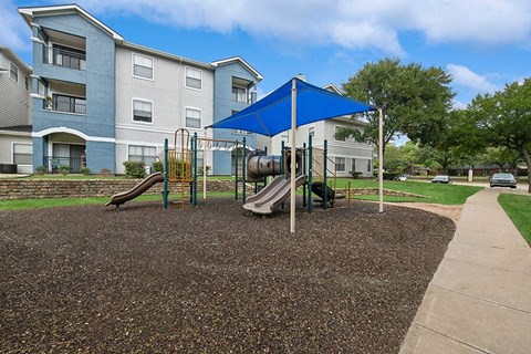 Community Playground with Slide and Blue Canopy at Hidden Creek Apartments located in Lewisville, TX.