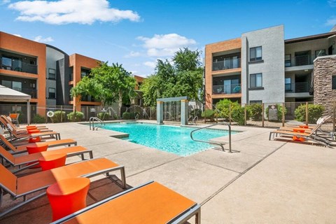 Surprise, AZ, Apartments with In-Unit Washer and Dryer - Harmony at Surprise - A Swimming Pool With Clear Blue Water, Orange Lounge Chairs, And View of Modern Apartment Buildings.