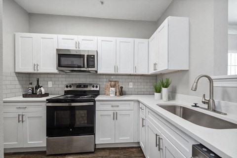 3-Bedroom Apartments in Lewisville, TX - Bridges at Oakbend - Kitchen With White Cabinets, Tile Backsplash, Stainless-Steel Appliances, Range With Microwave, And Double Sink With Sleek Faucet.