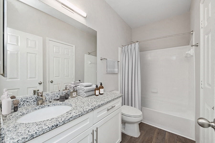 Model Bathroom with White Cabinets, Wood-Style Flooring and Shower/Tub at Chapel Hill Apartments in Lewisville, TX.