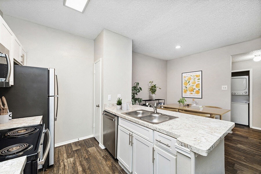 Model Kitchen with White Cabinets and Wood-Style Flooring with View of Dining Room at Dallas North Park Apartments in Dallas, TX.