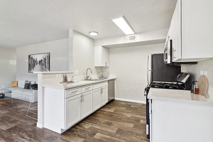 Model Kitchen with Wood-Style Flooring, White Cabinets and View of Living Room at Loma Vista Apartments in Las Vegas, NV.
