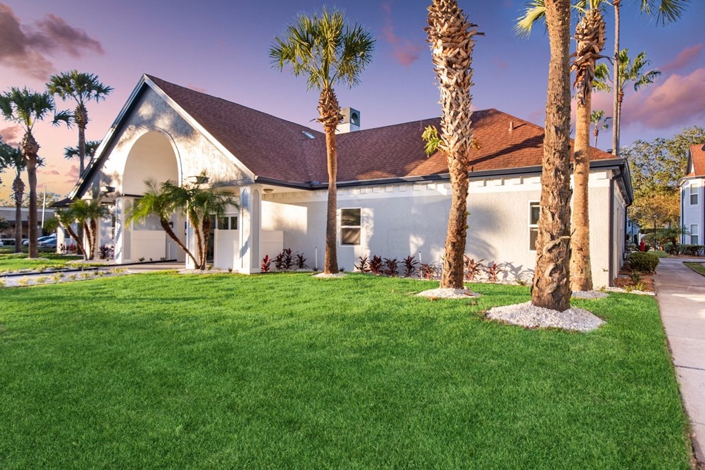 the front of a house with palm trees and grass