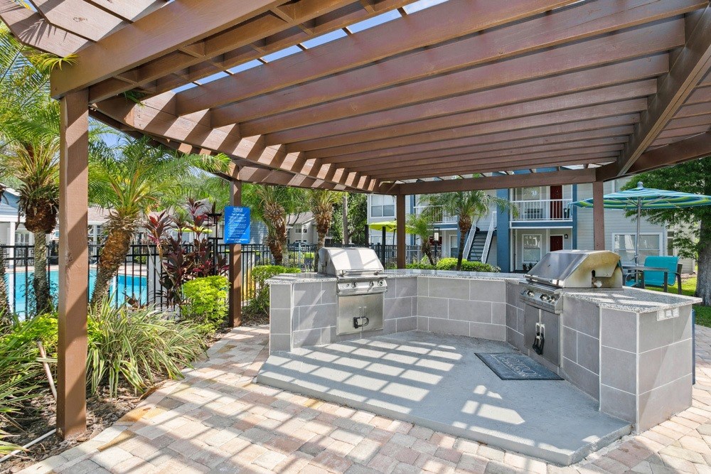Pergola with two barbecue grills and a pool in the background at Retreat at Crosstown Apartments