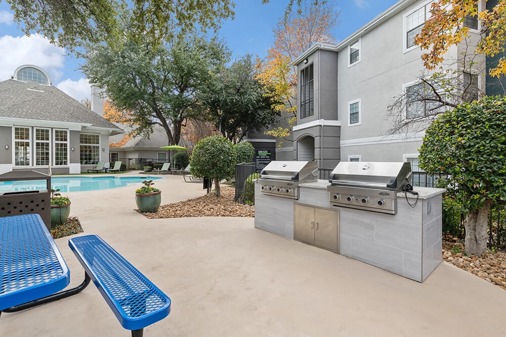 Outdoor BBQ Area with Furniture and Pool View at Bridges at Oakbend Apartments in Lewisville, TX.
