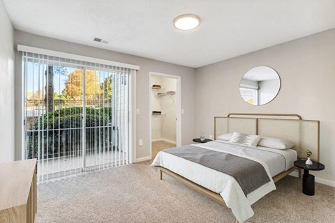 3-Bedroom Luxury Apartments in Jonesboro, GA - The Park at Tara Lake - A Bedroom With Large Sliding Glass Door, Neutral Carpet, Modern Bed With Side Tables, And Round Wall Mirror.