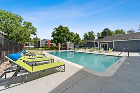 South Denver, CO, Apartments Near Kennedy Golf Course - Bridges at 9 Mile Station - A Swimming Pool Surrounded By Lounge Chairs, Trees, And Apartment Buildings.