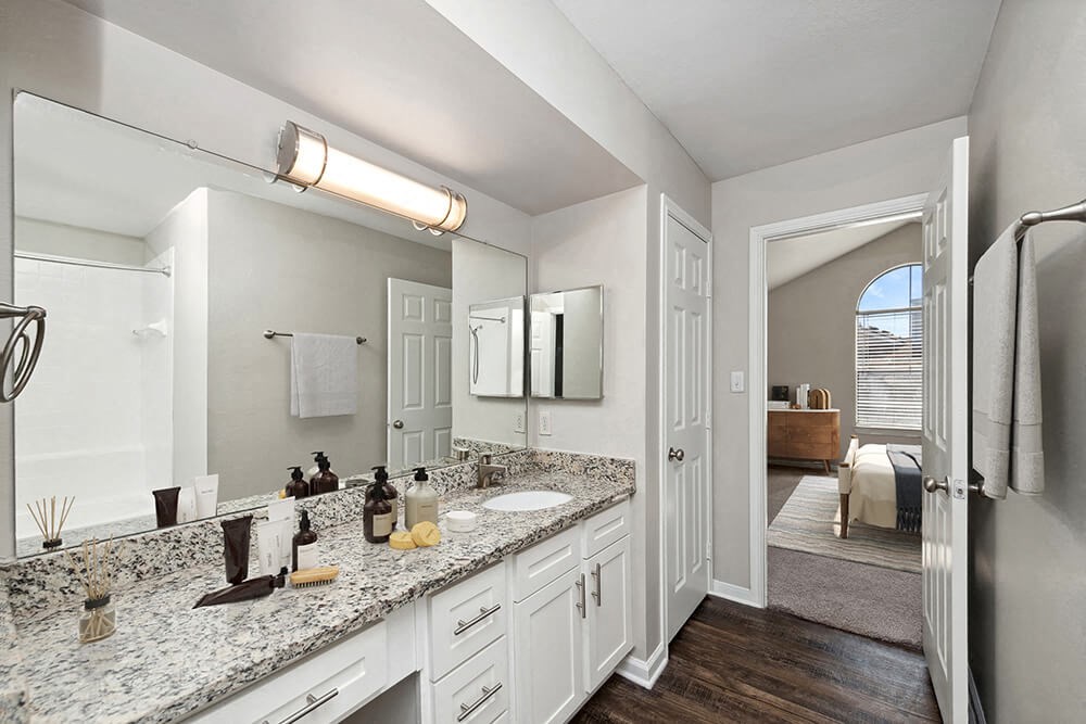 Model Bathroom with White Cabinets and Wood-Style Flooring at Hidden Creek Apartments in Lewisville, TX.
