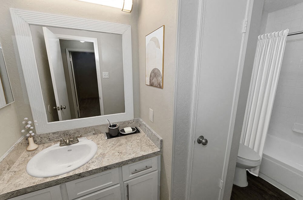 Model Bathroom with White Cabinets, Wood-Style Flooring and Shower/Tub at Dallas North Park Apartments in Dallas, TX.