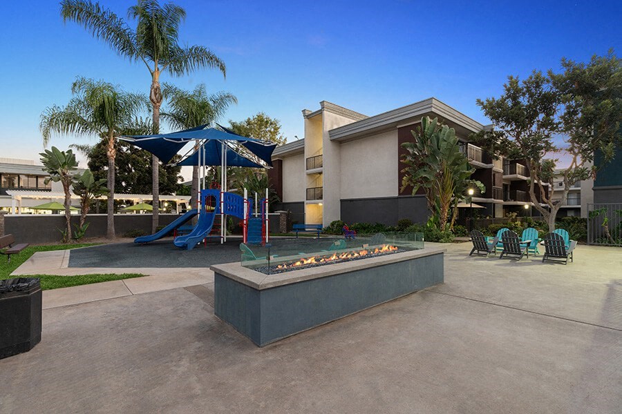 Community Fire Pit Area with Lounge Furniture and View of Playground at Madison Park Apartments located in Anaheim, CA.