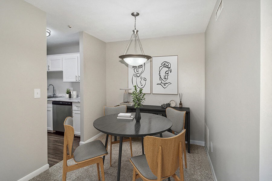 Model dining area with a table and chairs and kitchen in the background  at Stone Ends apartments in Stoughton, MA
