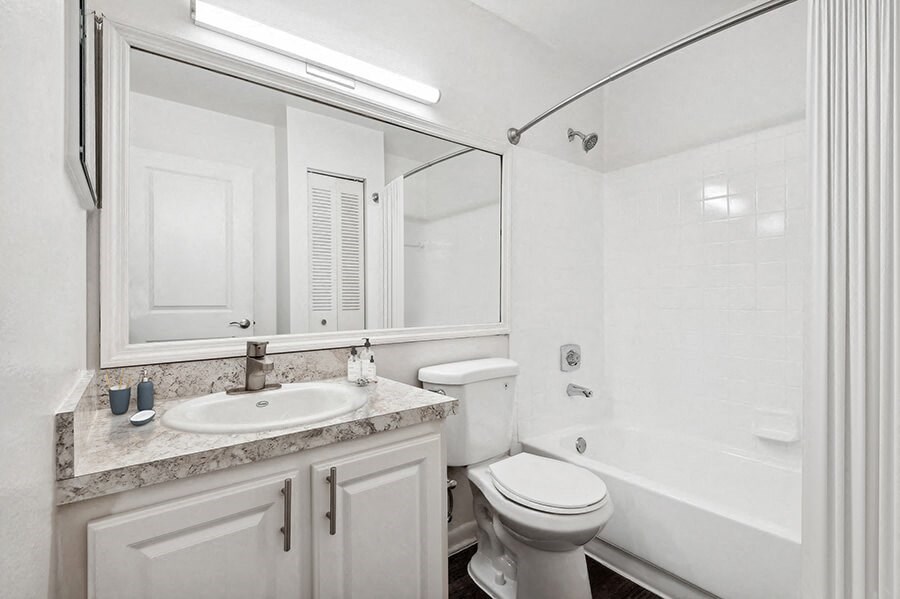 Model Bathroom with Wood-Style Flooring, White Cabinets & Shower/Tub at Rosehill Preserve Apartments located in Orlando, FL.