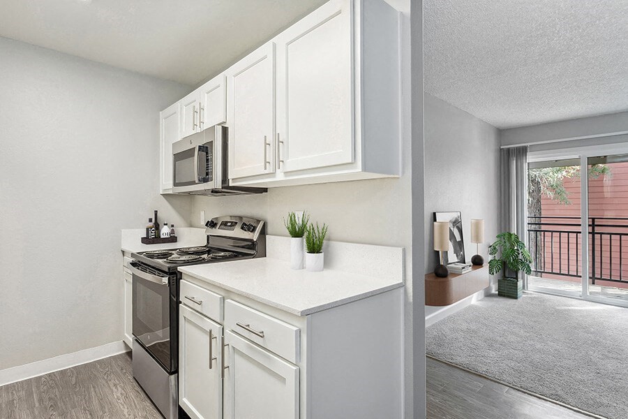 Model Kitchen with White Cabinets, Wood-Style Flooring and Living Room View at The Archer Apartments in Sacramento, CA.