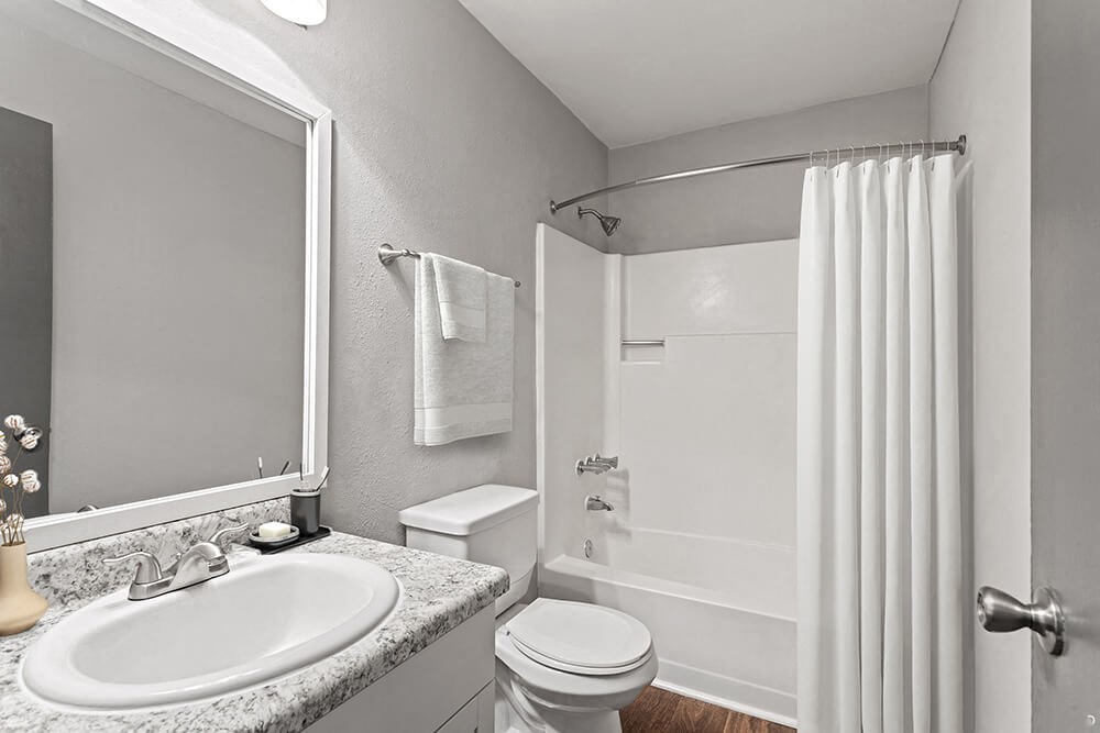 Model Bathroom with White Cabinets, Wood-Style Flooring and Shower/Tub at Corners at 1700 Apartments in Atlanta, GA.