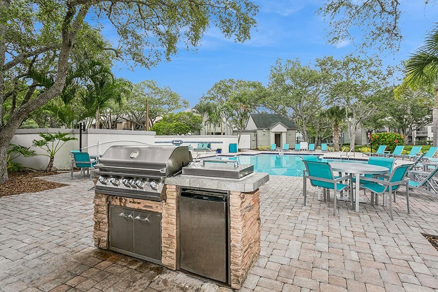 Outdoor BBQ Area with Lounge Furniture and View of Swimming Pool at Huntington Place Apartments located in Sarasota, FL.