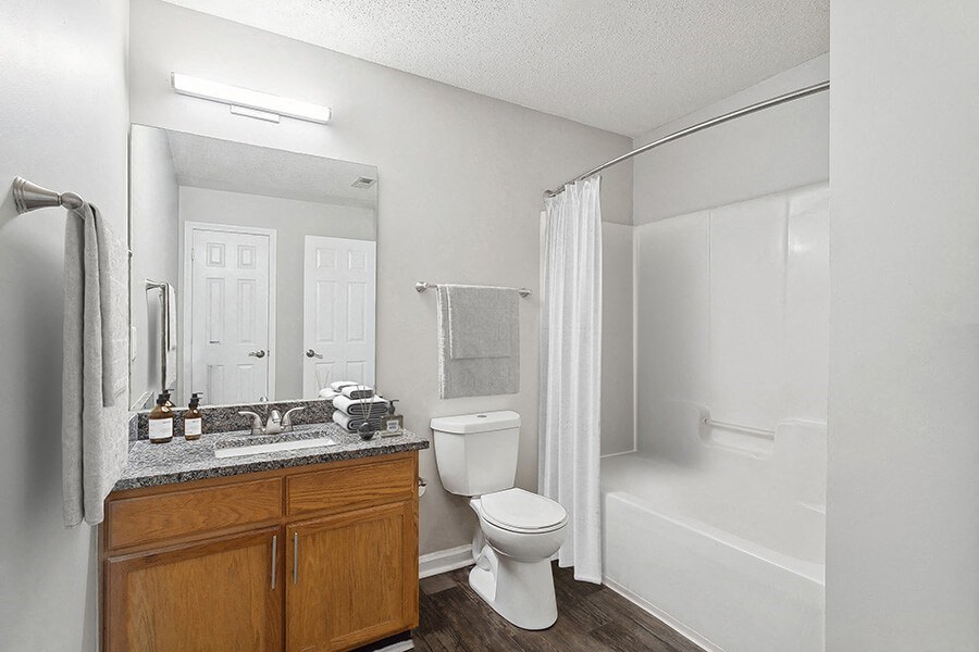 Model Bathroom with Wood-Style Flooring, Oak Cabinets and Shower/Tub at Retreat at Stonecrest Apartments located in Lithonia, GA.