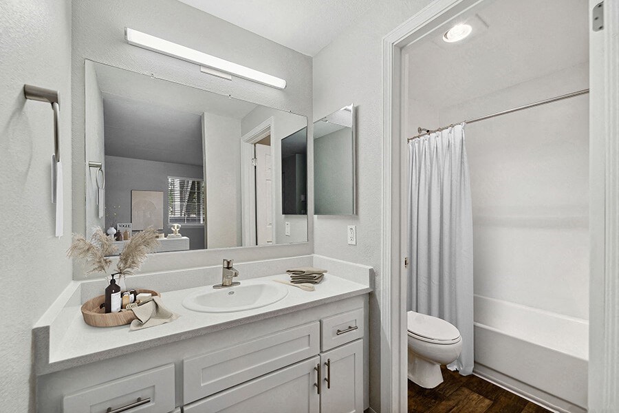 Model Bathroom with White Cabinets, Wood-Style Flooring and Shower/Tub at Central Flats Apartments in Kent, WA.