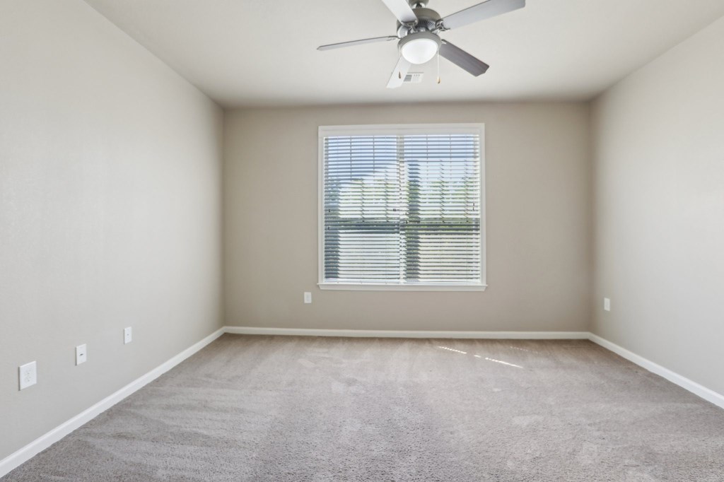Model bedroom with a ceiling fan and a window with blinds.