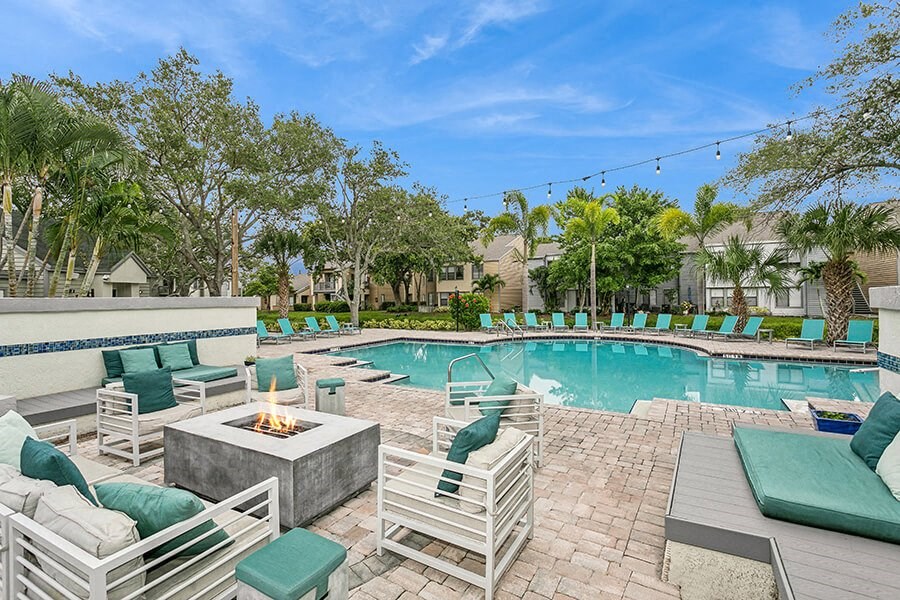 Outdoor Fire Pit Area and Swimming Pool with Lounge Furniture at Huntington Place Apartments located in Sarasota, FL.