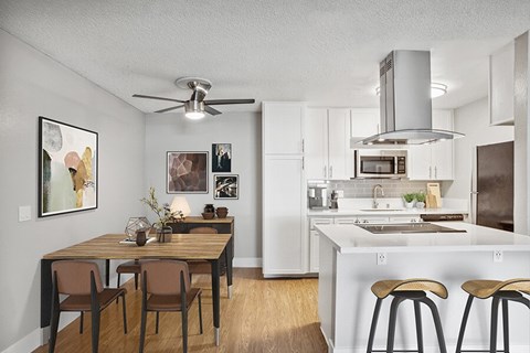 A kitchen with a table and chairs in the foreground and a stove top oven in the background.