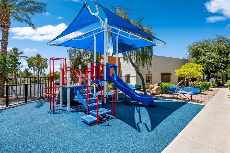 Community Playground with a Slide and Blue Canopy at Harmony at Surprise Apartments in Surprise, AZ.