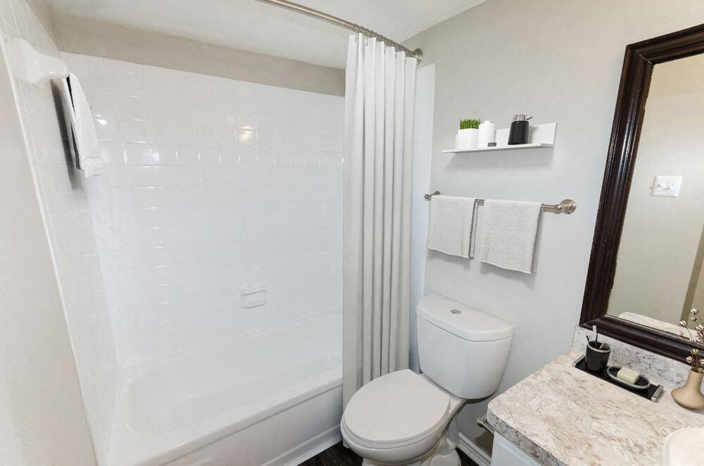 Model Bathroom with White Cabinets, Wood-Style Flooring and Shower/Tub at Cobblestone Apartments in Arlington, TX.