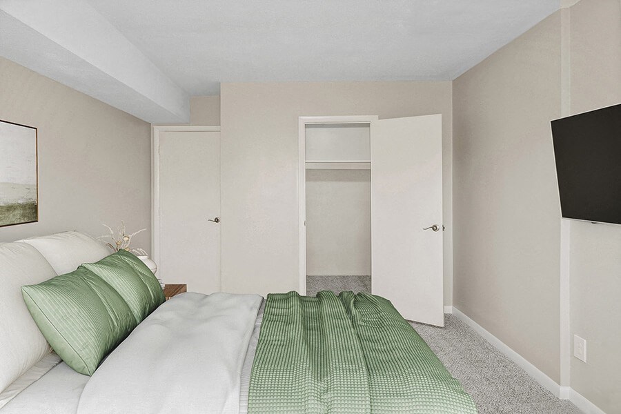 Model bedroom with a bed and a door to a closet  at Stone Ends apartments in Stoughton, MA