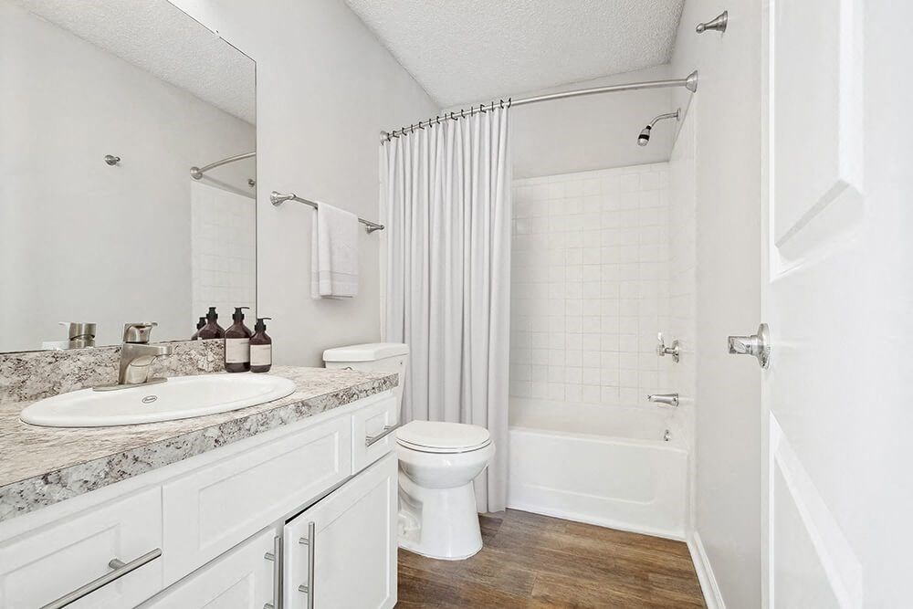 Model Bathroom with White Cabinets, Wood-Style Flooring and Shower/Tub at Westland Park Apartments in Jacksonville, FL.