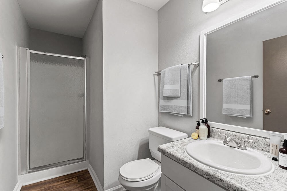 Model Bathroom with White Cabinets, Wood-Style Flooring and Standing Shower at Corners at 1700 Apartments in Atlanta, GA.