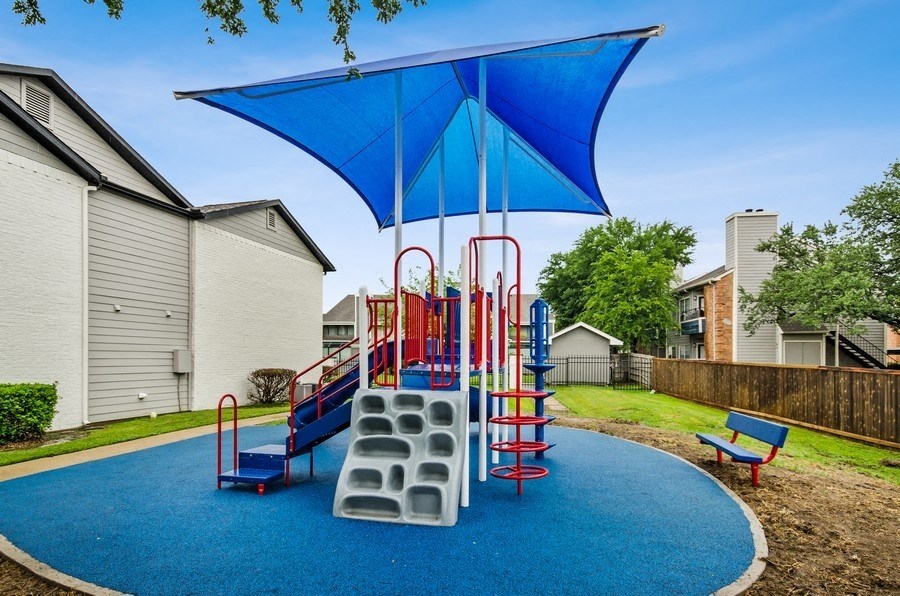 a playground with a swing set and a blue umbrella