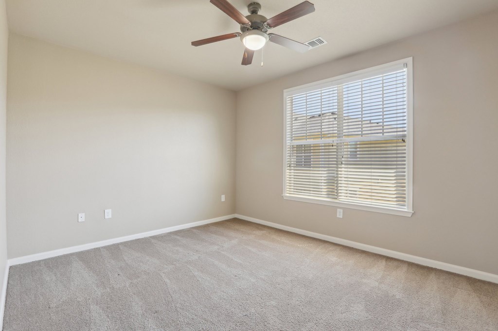 Model bedroom with a ceiling fan and a window with blinds.