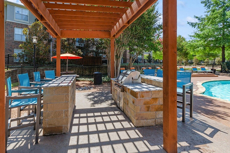 Outdoor BBQ Area with Furniture and Pool View at Belmont at Duck Creek Apartments in Garland, TX.