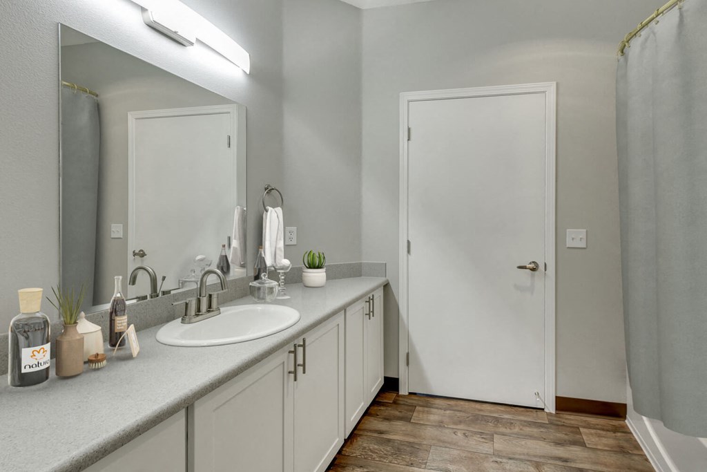 Model Bathroom with White Cabinets, Wood-Style Flooring and Shower/Tub at Landings at Morrison Apartments located in Gresham, OR.
